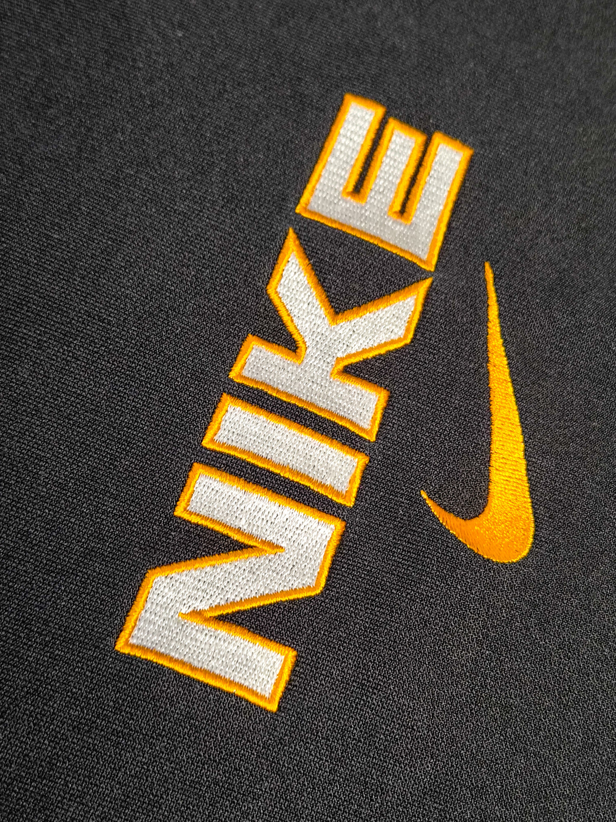 Close up van het NIKE logo op de voorkant inclusief swoosh. Oranje omlijning en witte letters.