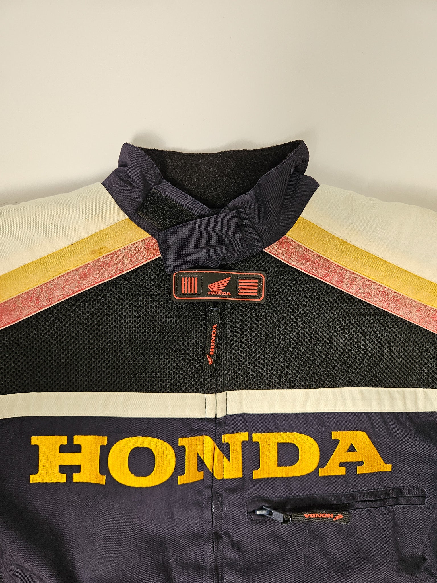 Detail van het Honda Racing logo en teampatches op de borst van de jas, met zichtbare slijtage van gebruik

