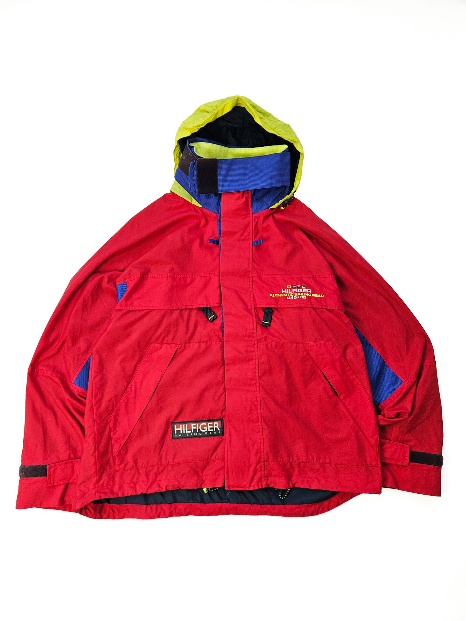 1990s Tommy Hilfiger Sailing Gear vintage jas in rood met blauwe en gele panelen en neon capuchon, vooraanzicht flatlay