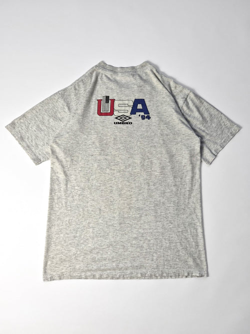 Achterkant van het grijze vintage Umbro T-shirt met een kleine rood-wit-blauwe USA ’94-print en zwart Umbro-logo.
