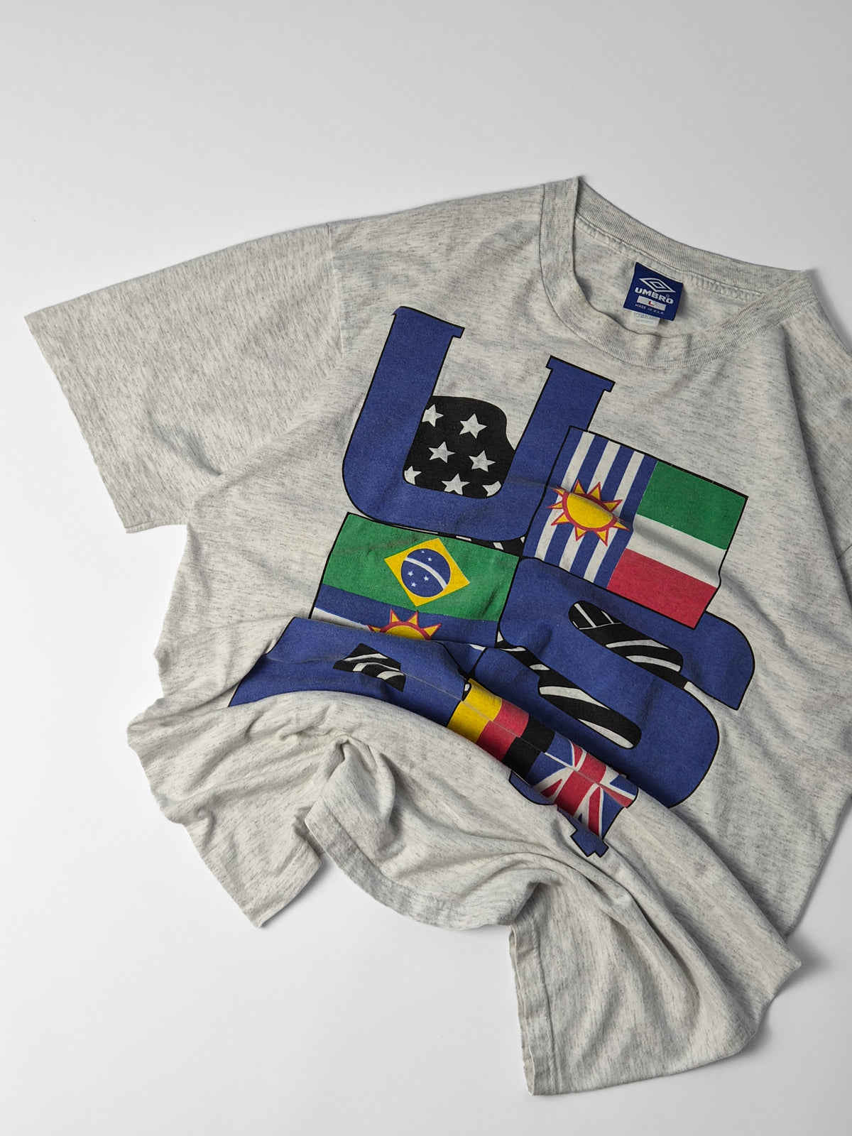 Schuin neergelegd Umbro USA ’94 T-shirt met de grote vlaggenprint, ronde hals en ruime korte mouwen in beeld.