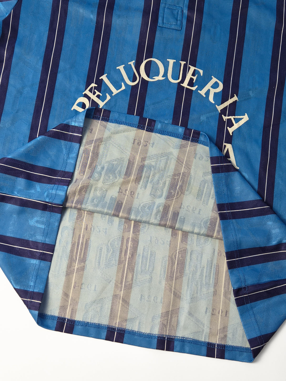 Vintage Umbro voetbalshirt uit de jaren '90 in blauw met gestreepte all-over print en Peluquería Maluisa borstprint opengeklapt.