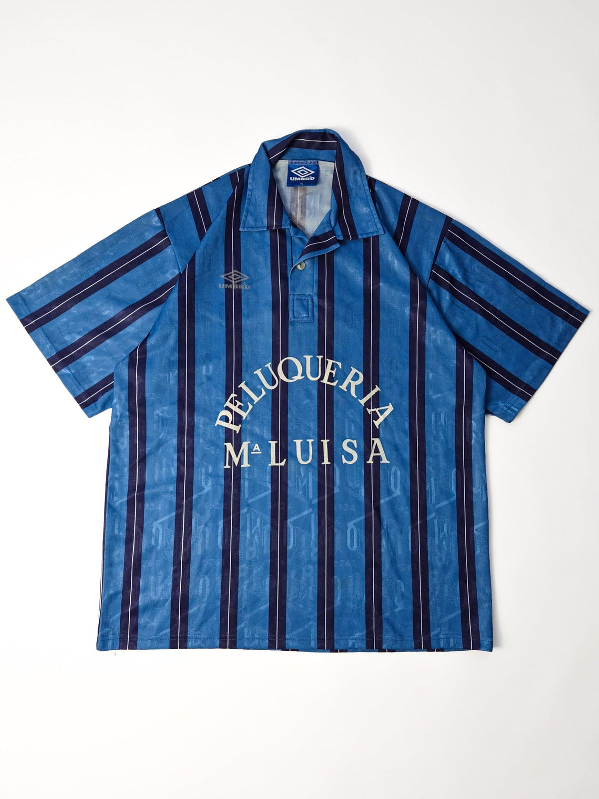 Vintage Umbro voetbalshirt uit de jaren '90 in blauw en navy met Peluquería Maluisa sponsor, voorkant flatlay.
