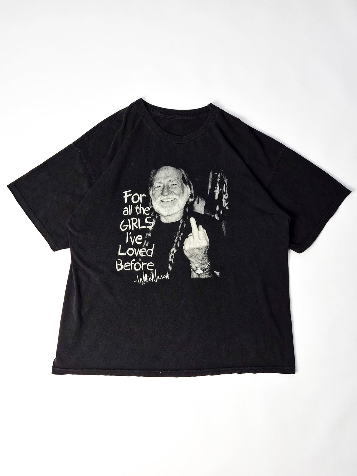 Vintage Willie Nelson T-shirt uit circa 2000 in faded zwart met grote zwart-witte outlaw country graphic, volledig plat gefotografeerd.