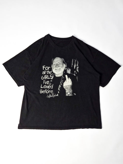 Vintage Willie Nelson T-shirt uit circa 2000 in faded zwart met grote zwart-witte outlaw country graphic, volledig plat gefotografeerd.